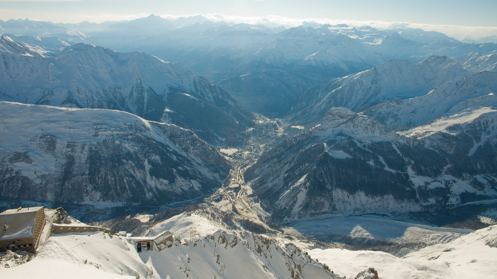 The view into a snowy valley from a mountain top. Colours in white and blues.