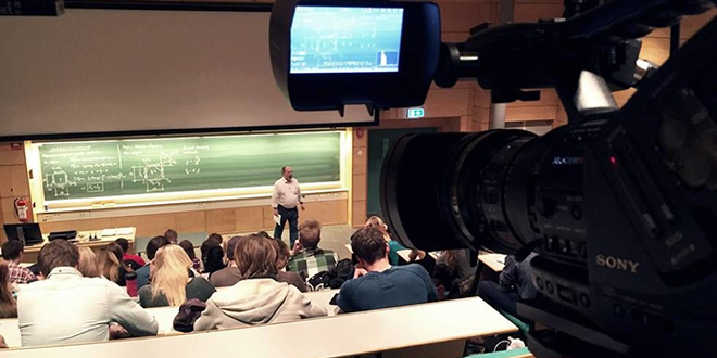 studenter sitter i et auditorium og får undervisning av en professor. Forelesningen blir filmet.