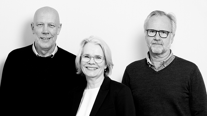 tre personer stårforan en lys vegg, ser i kamera