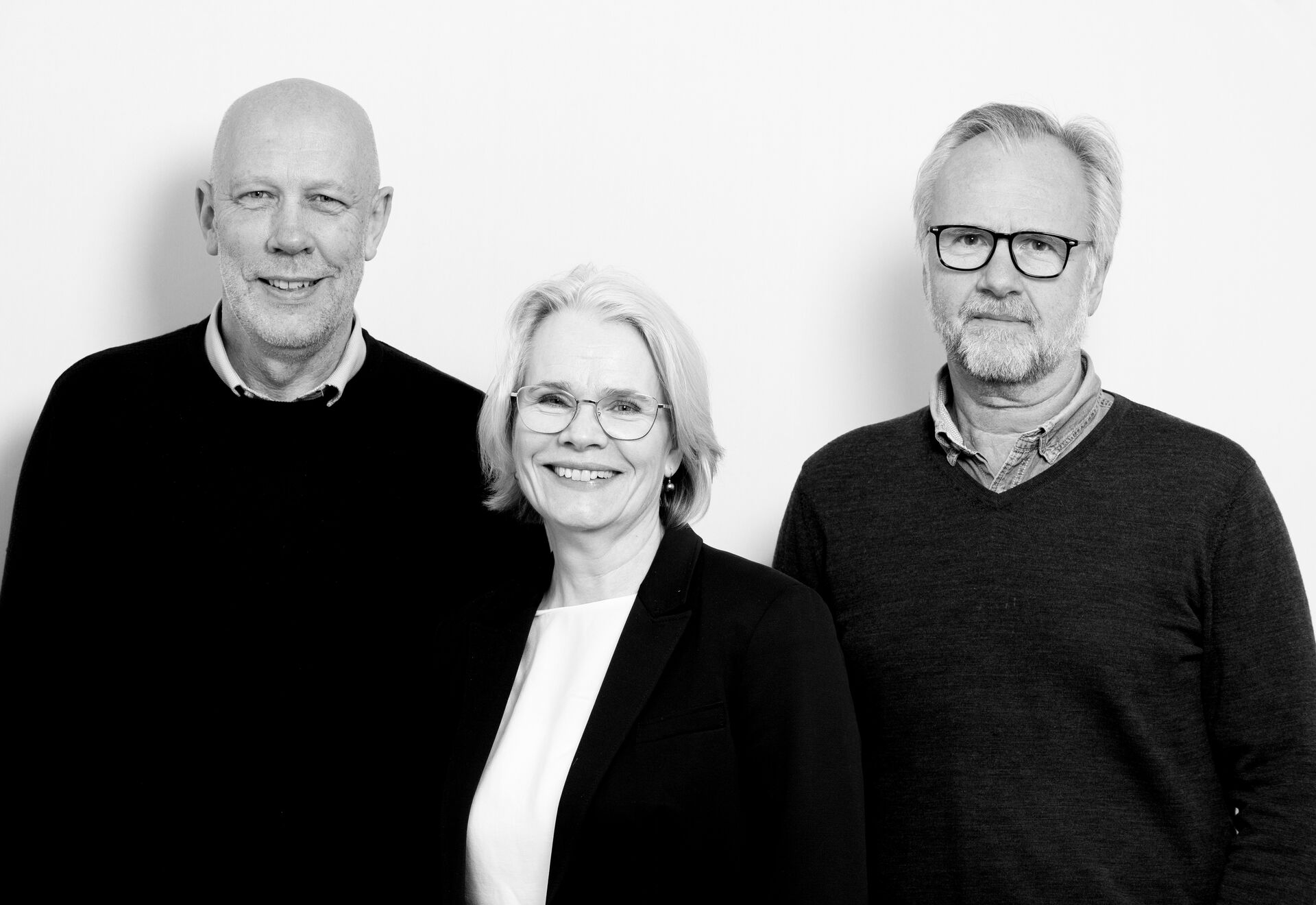 tre personer står foran en vegg, ser i kamera