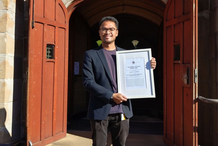 Amando Lasabuda holding the award certificate in front of the Madsen Building, University of Sydney