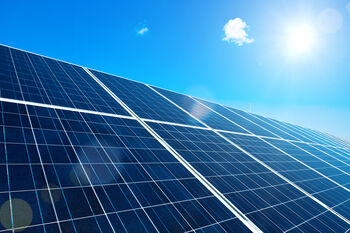 Image of solar cells and a clear blue sky. From the top right corner the sun shines bright on the solarcells. 
