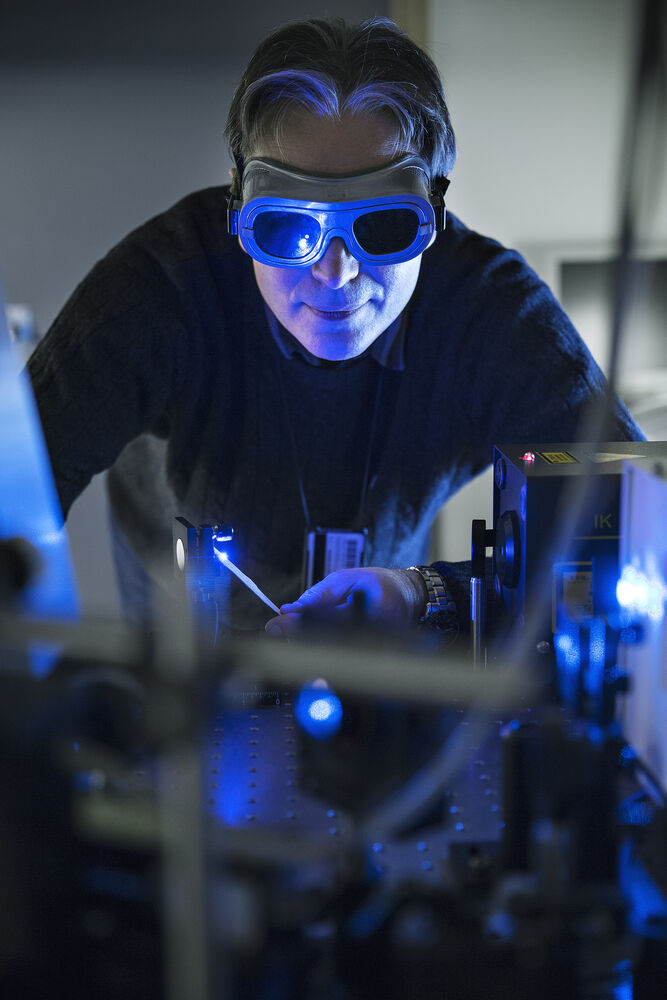 Researcher, Augustinas Galeckas, wearing safety glasses. The researcher is pointing a blue laser towards the camera. 