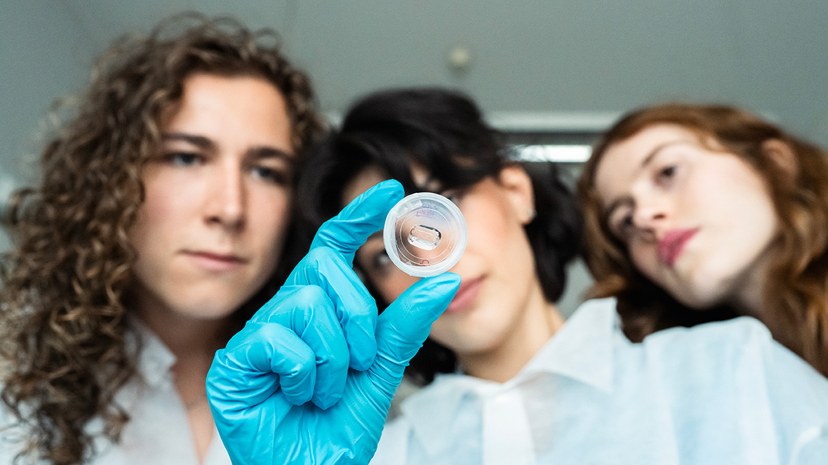 Close-up of three students in lab coats looking at a drop in a small container