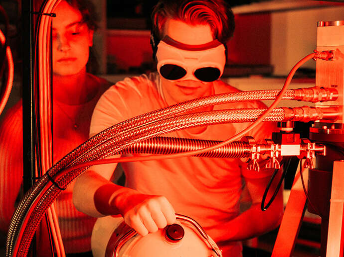 To studenter opererer utstyr i laboratorium; vernebriller