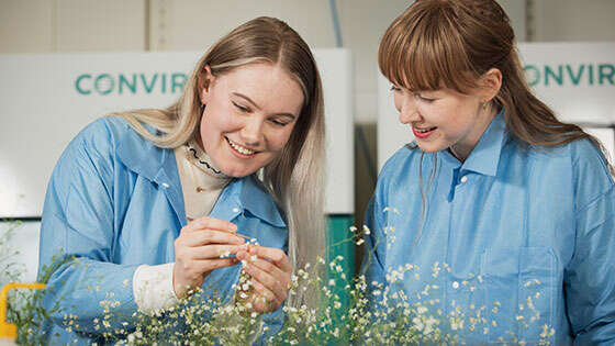 To kvinnelige studenter i labdrakt som studerer en plante