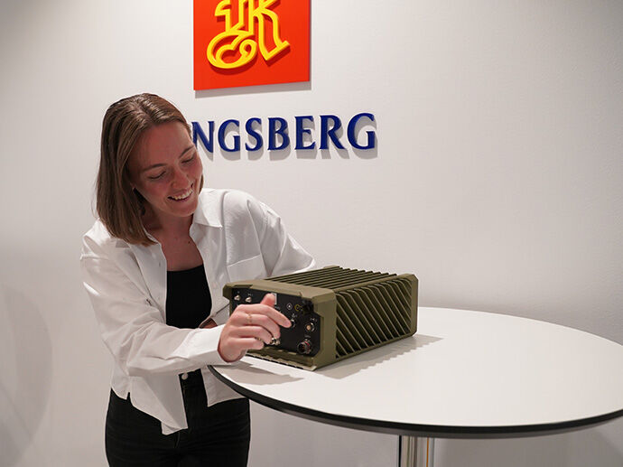 Ung dame med mellomkort brunt hår og hvit skjorte skurr på en radio fra forsvaret som heter Thor.